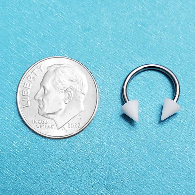 A white spike septum ring pictured on an aqua background next to a dime for a size comparison.